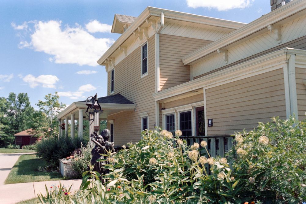 A beige two-story house with landscaped flower gardens along the front walkway.
