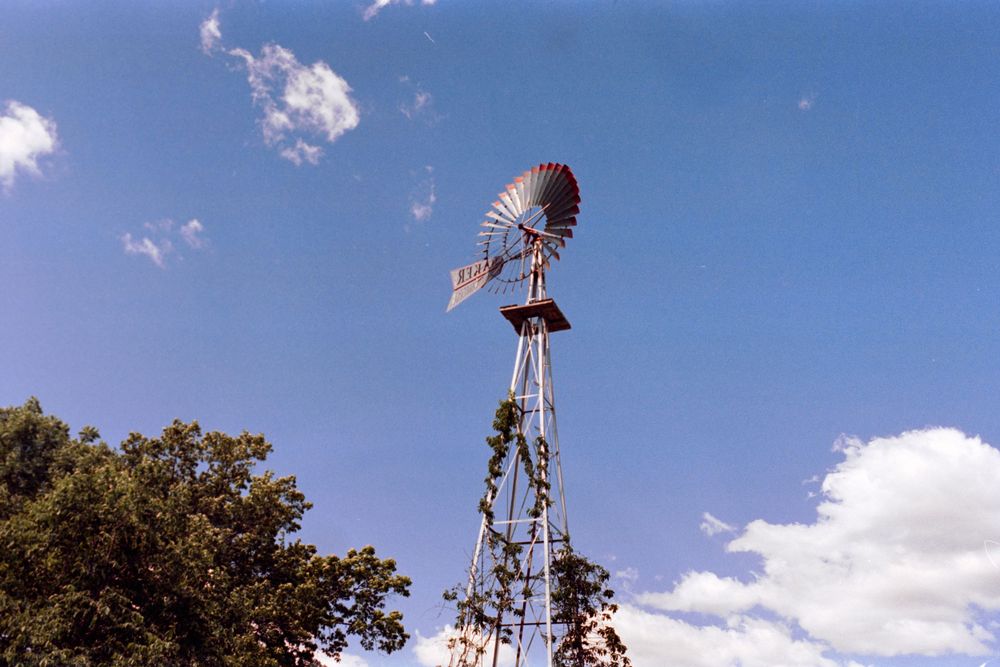 A tall metal windmill stands against a bright blue sky with white puffy clouds.