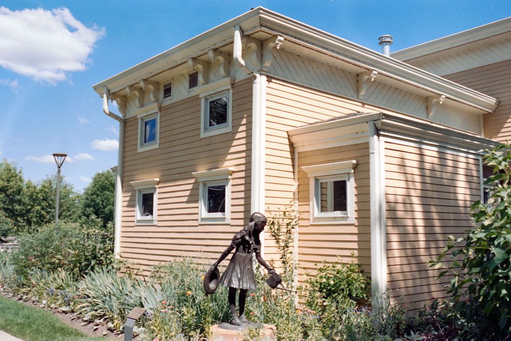 Modern tan-colored house with multiple windows and architectural details surrounded by landscaping.
