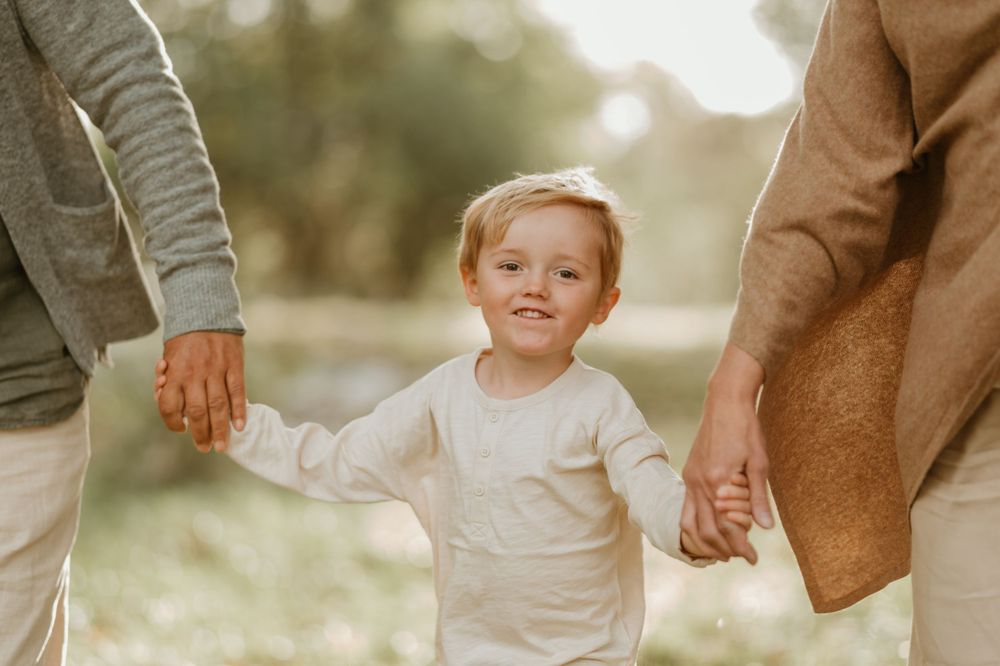 A small child holds hands with adults while walking outdoors on a sunny day.
