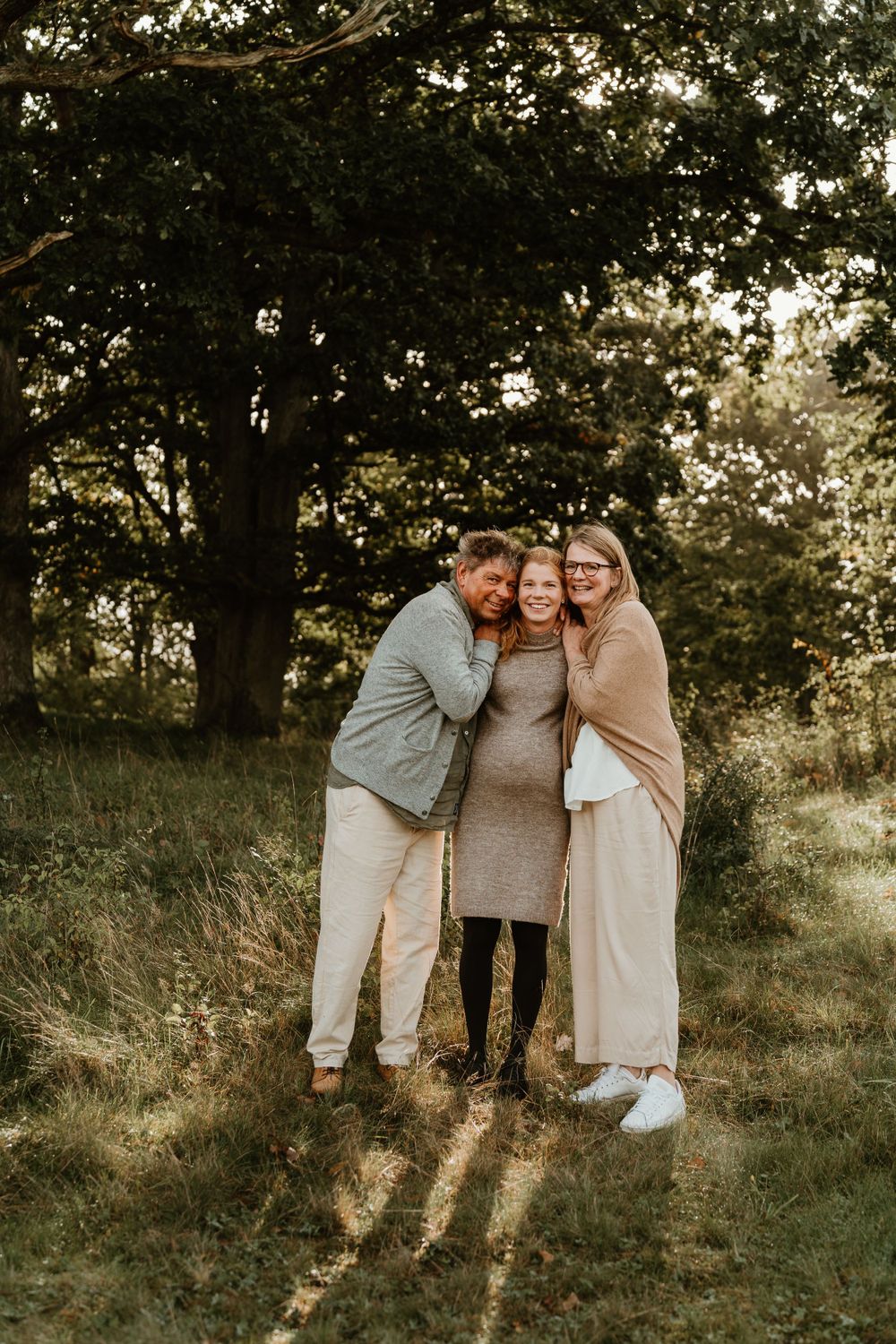Three people embrace while sharing a happy moment in a sunlit meadow.