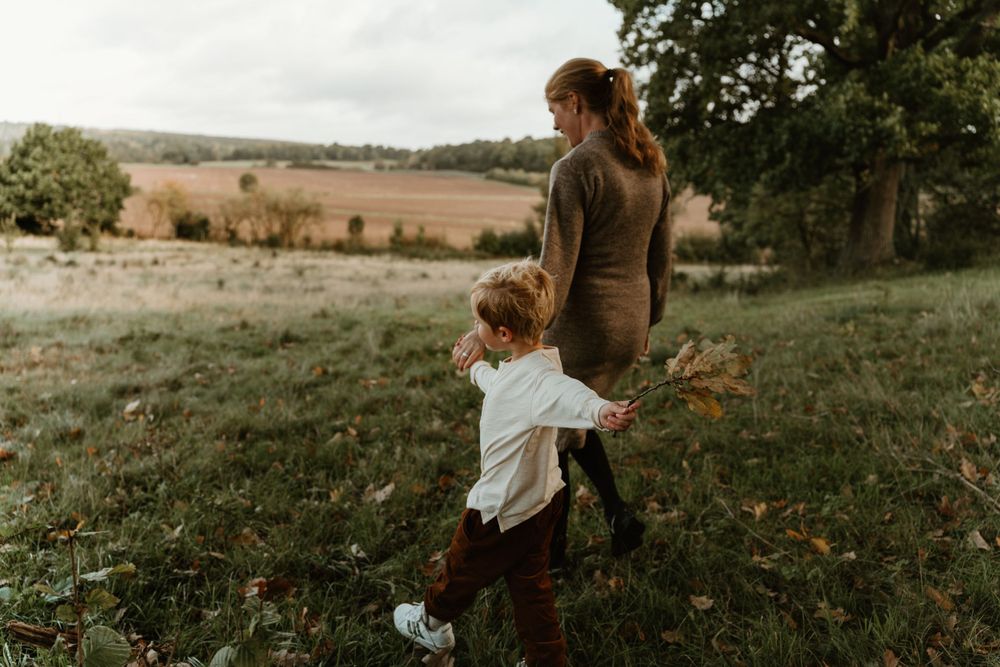 A parent and child walk together through an autumn field at sunset.