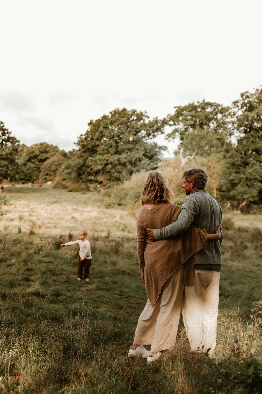 Two people embrace while watching a child play in a distant meadow.