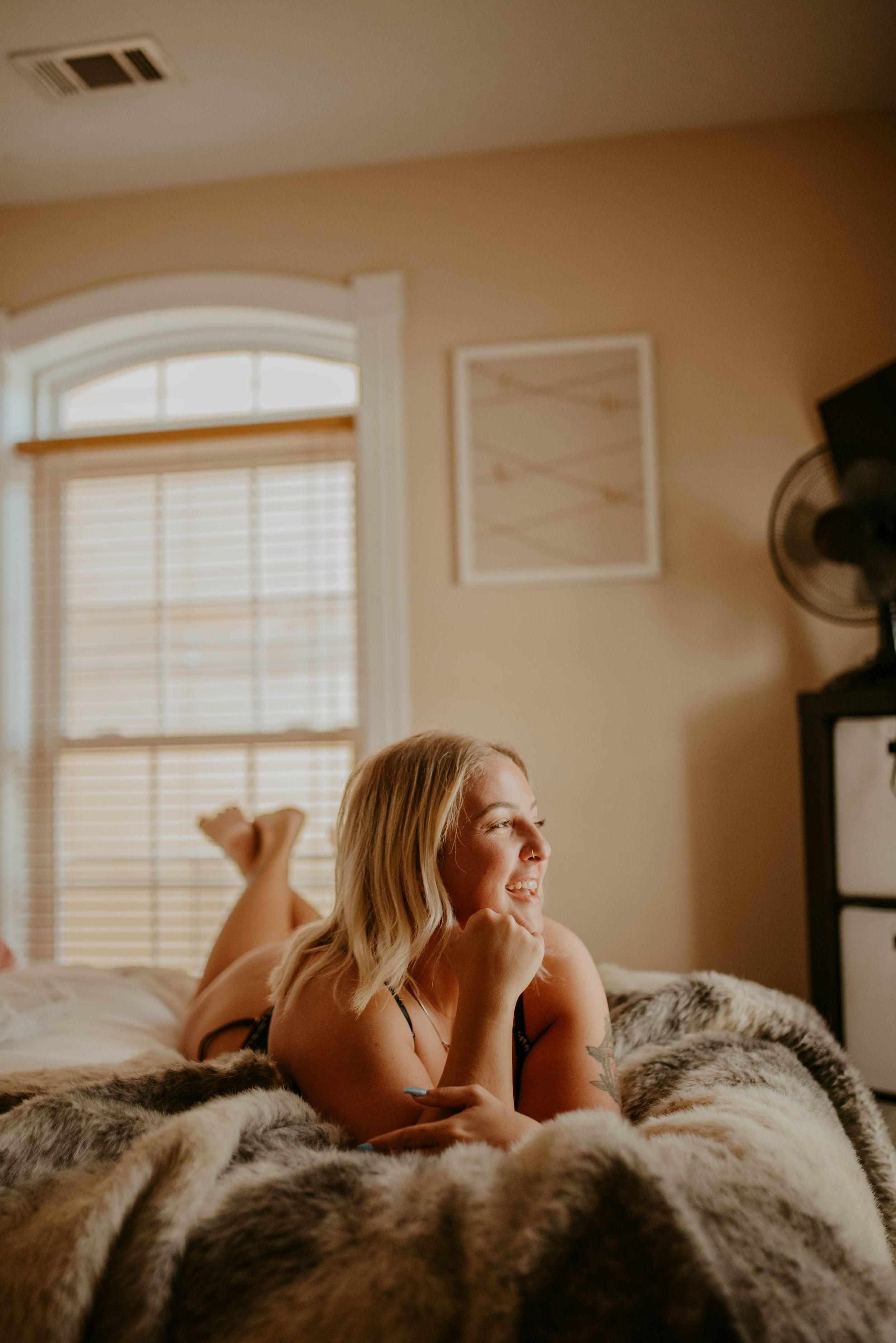 Intimate boudoir photography session on plush fur blanket with natural window lighting.