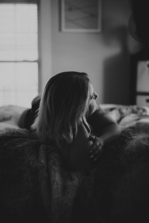 Moody black and white portrait with window light creating dramatic shadows.