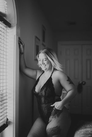 Natural light boudoir photo showing joyful expression by window.