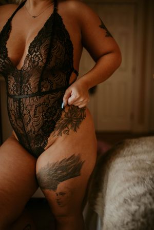 Close-up boudoir photo showcasing intricate lace bodysuit and detailed tattoo artwork.