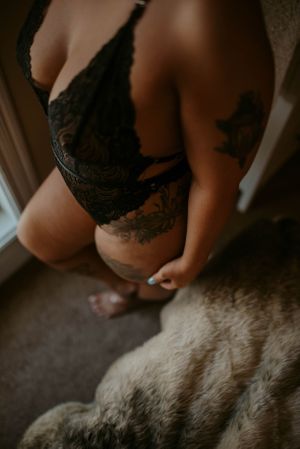 Close-up of black lace lingerie against skin with tattoo detail on a furry blanket.