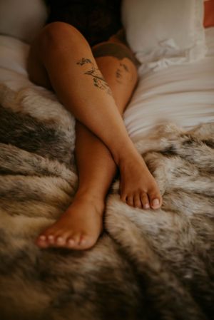 Close-up of tattooed legs resting on plush faux fur blanket in warm tones.