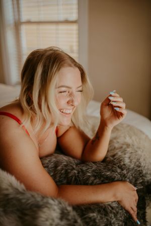 Woman relaxing on gray faux fur bedding with a joyful expression.