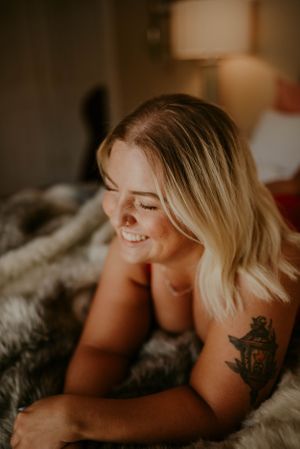 Warm-toned portrait showcasing tattoo artwork and genuine smile on plush bedding.