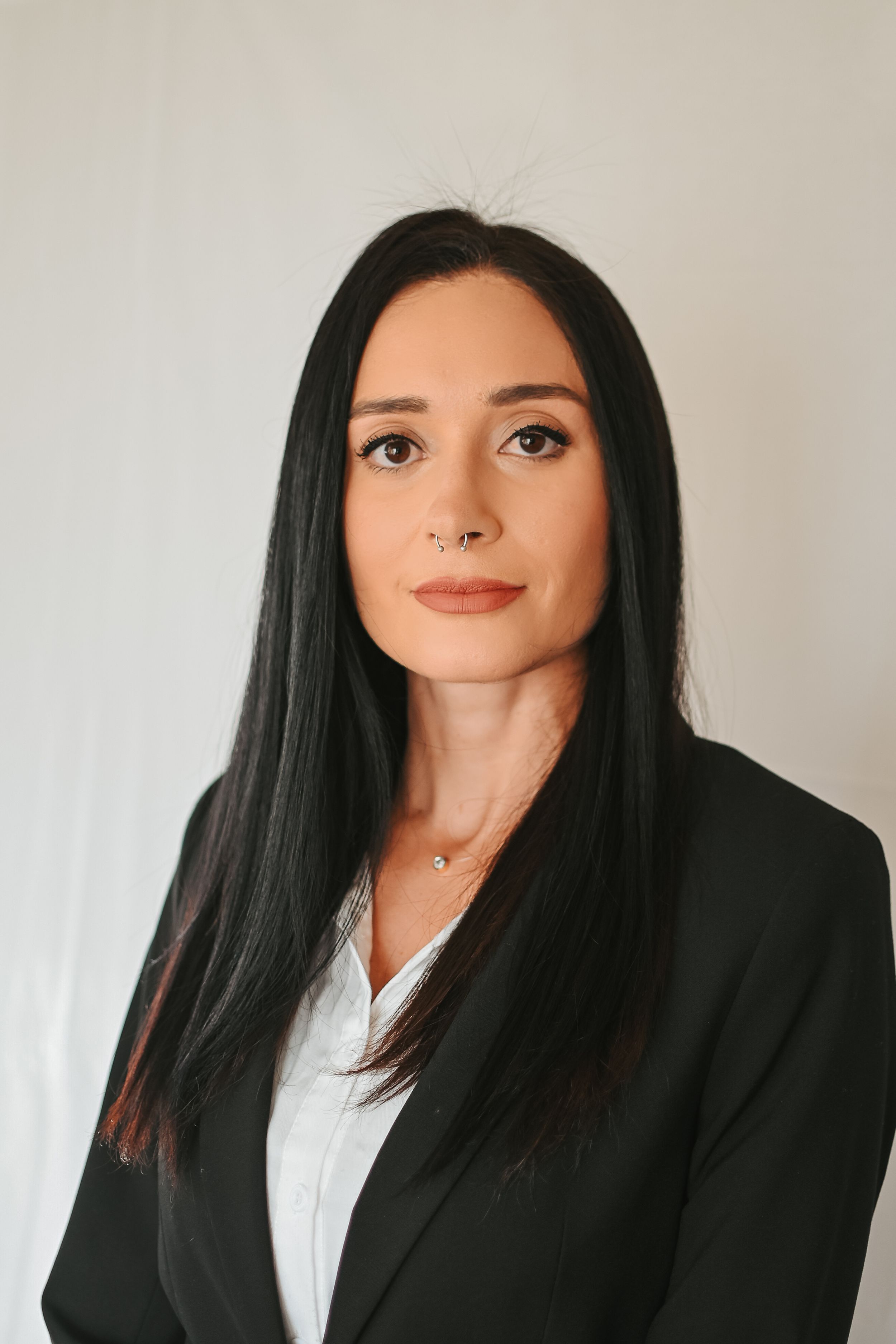 Professional headshot against white background wearing black blazer and white blouse.