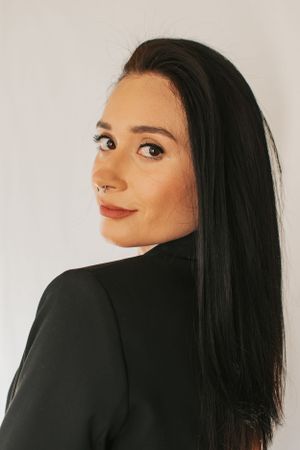 Side profile portrait with long dark hair against white backdrop wearing black blazer.