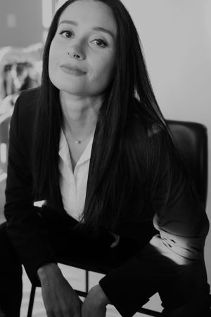 Professional portrait of a business professional in black blazer and white shirt against light background.