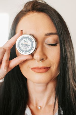 Artistic product photo showing silver container held against closed eyes.