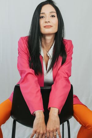 Dynamic fashion poses in pink blazer and orange pants while seated on black chair.