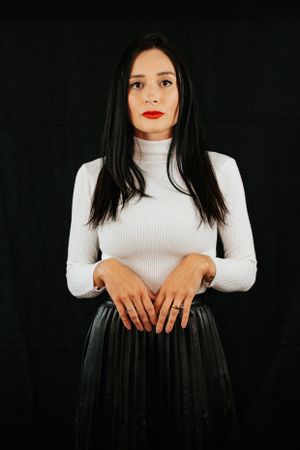 Dramatic portrait in white turtleneck and black skirt against dark background.