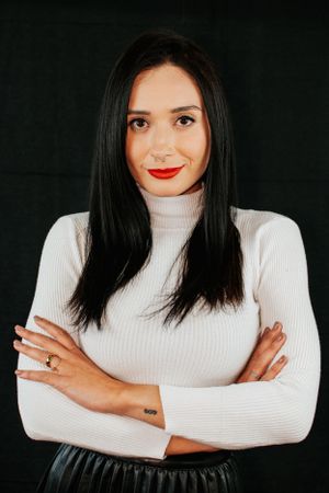 Fashion portrait series in white ribbed turtleneck against black background with crossed arms poses.