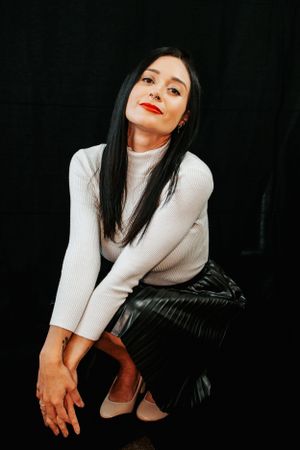 Artistic fashion poses in white turtleneck and black skirt against dark backdrop.