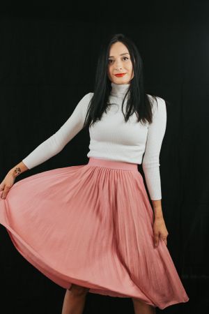 Stylish outfit featuring white turtleneck and flowing pink midi skirt against dark backdrop.