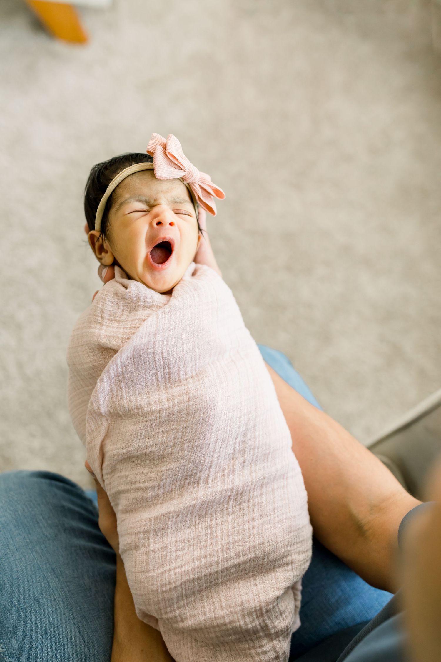 Swaddled baby yawning while wearing a pink bow headband.