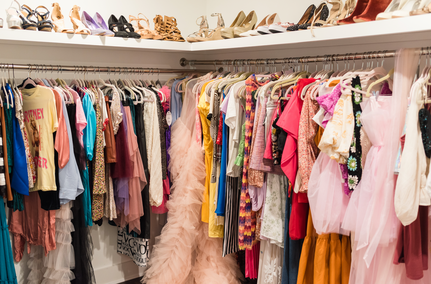 Panoramic view of a closet filled with colorful dresses, shoes, and clothing on hangers.