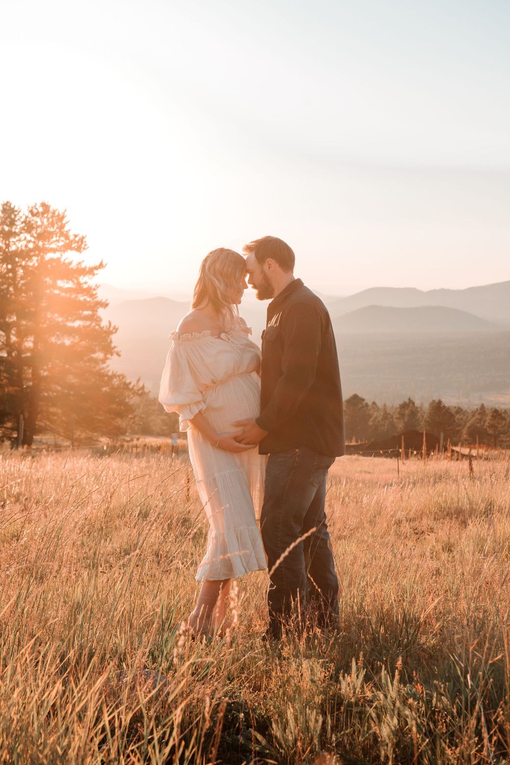 Couple shares an intimate moment in a sun-drenched mountain meadow at sunset.