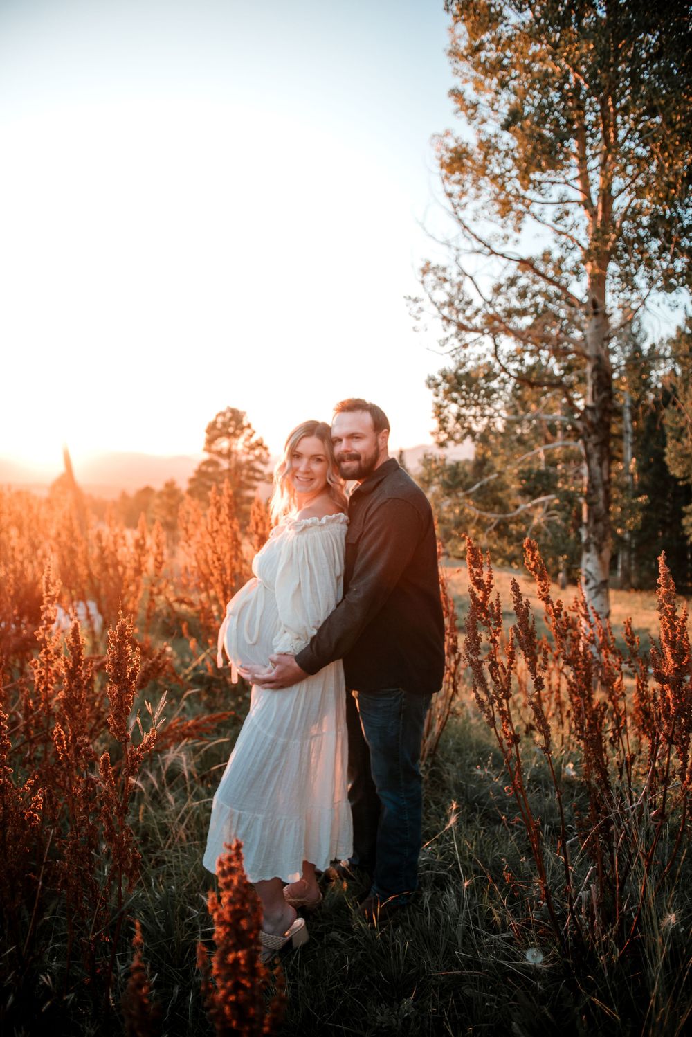 Intimate moment captured between couple in white dress and dark clothing among sunset-lit wildflowers.