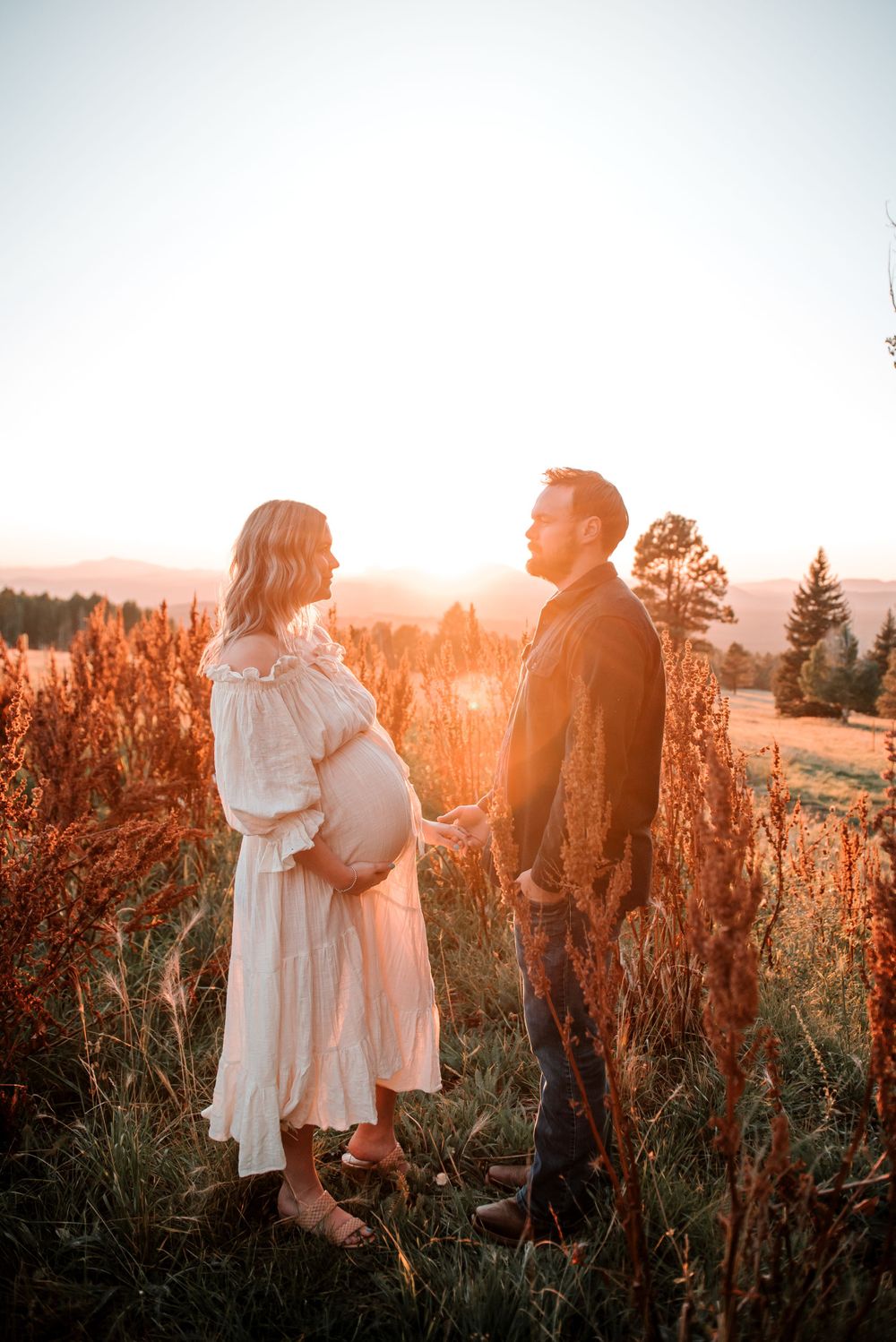 Couple shares tender moment in field of tall red flowers during magical sunset.
