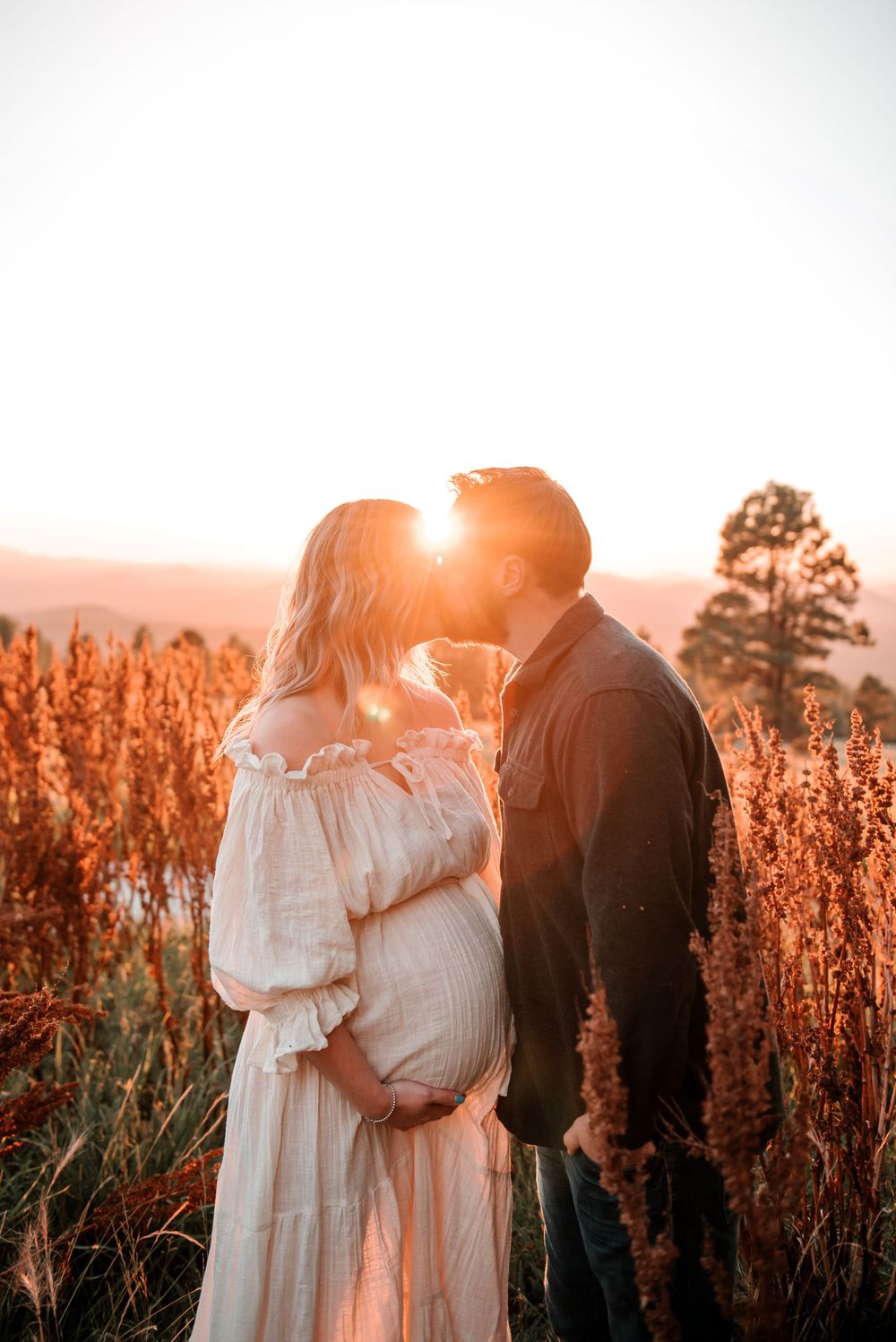 Warm sunset light illuminates couple's embrace among tall red wildflowers.