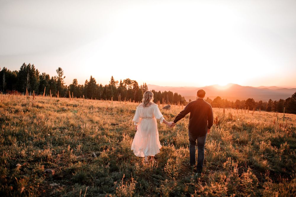 Silhouetted couple walks hand in hand through mountain meadow at sunset.
