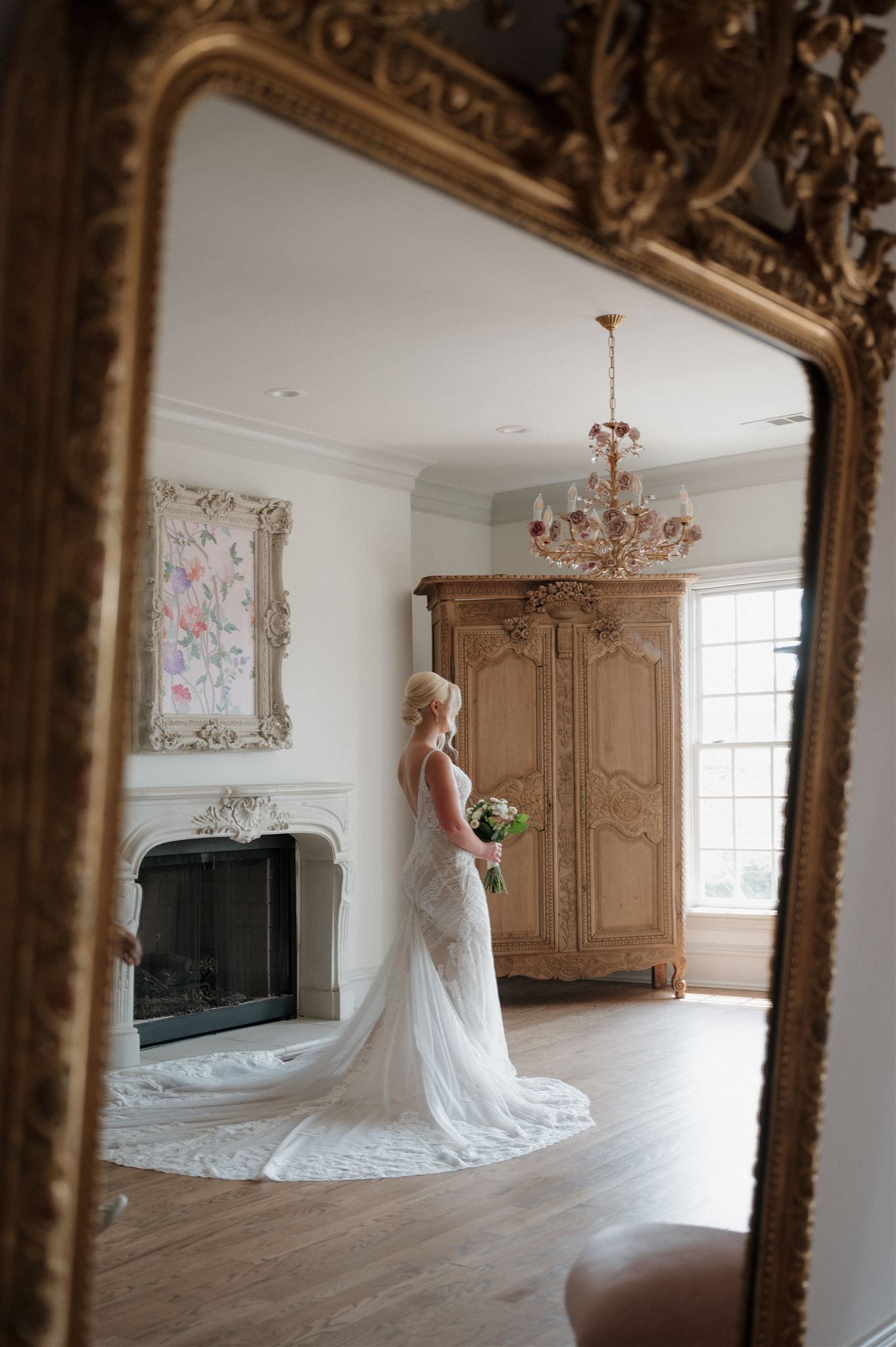 Mirror reflection captures bridal portrait in elegant room with vintage furniture and fireplace.