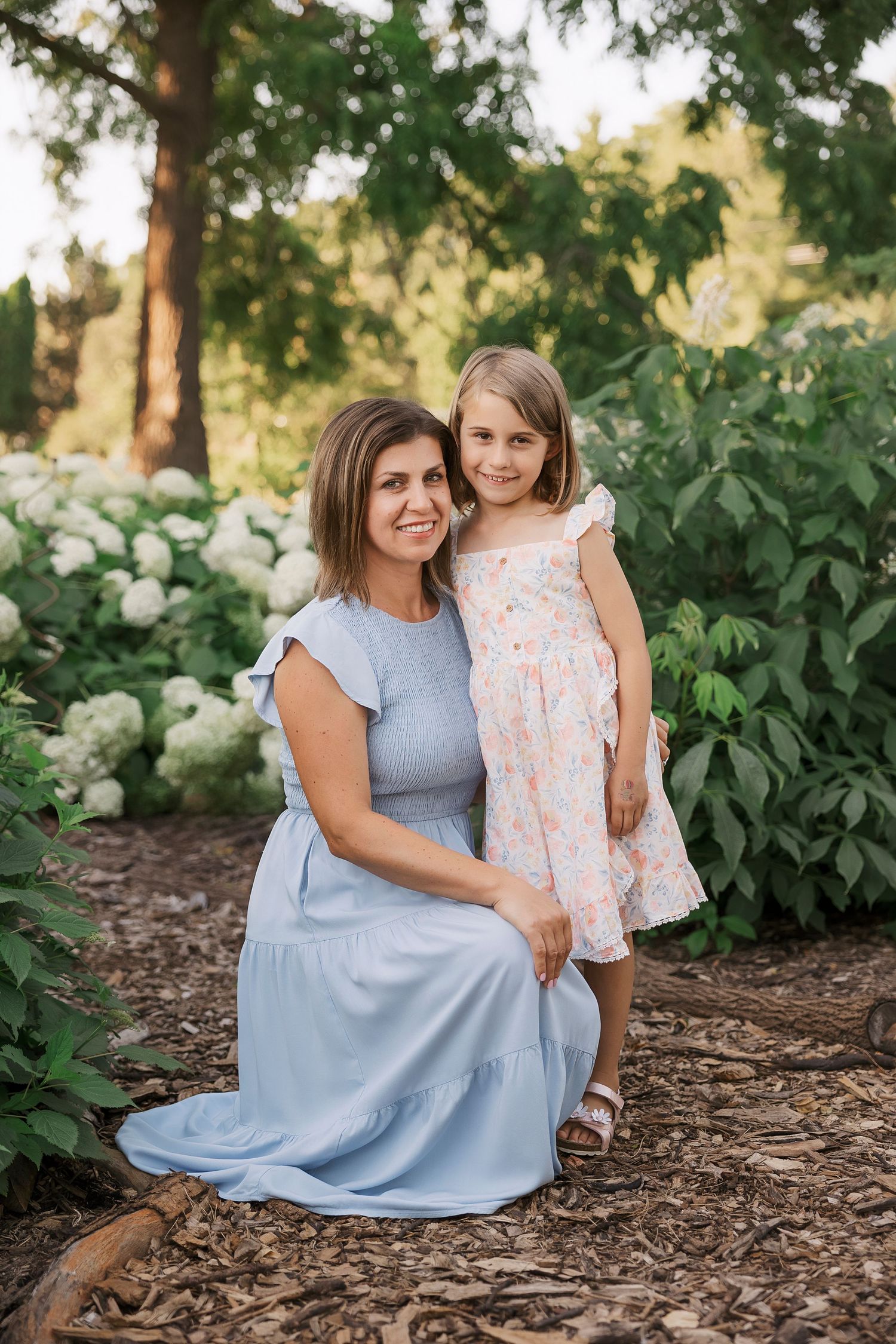 Two people pose together among white hydrangea bushes in garden setting.