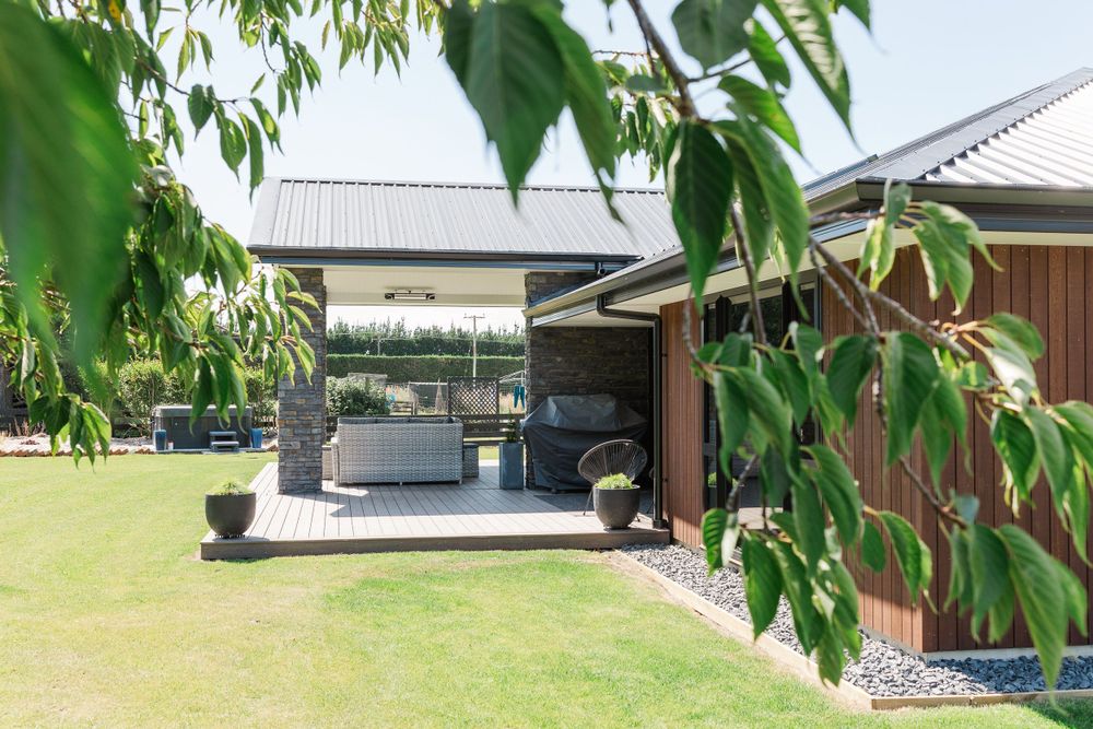 Modern outdoor patio area with comfortable seating under a covered pergola surrounded by green lawn.