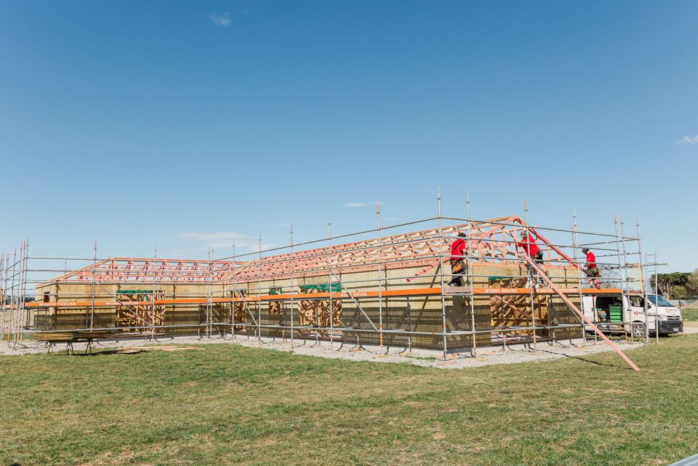 Wide view of residential construction site with scaffolding and timber frame structure.