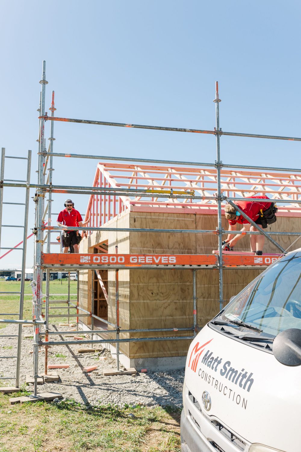Construction workers on scaffolding work on installing roof trusses at a residential building site.