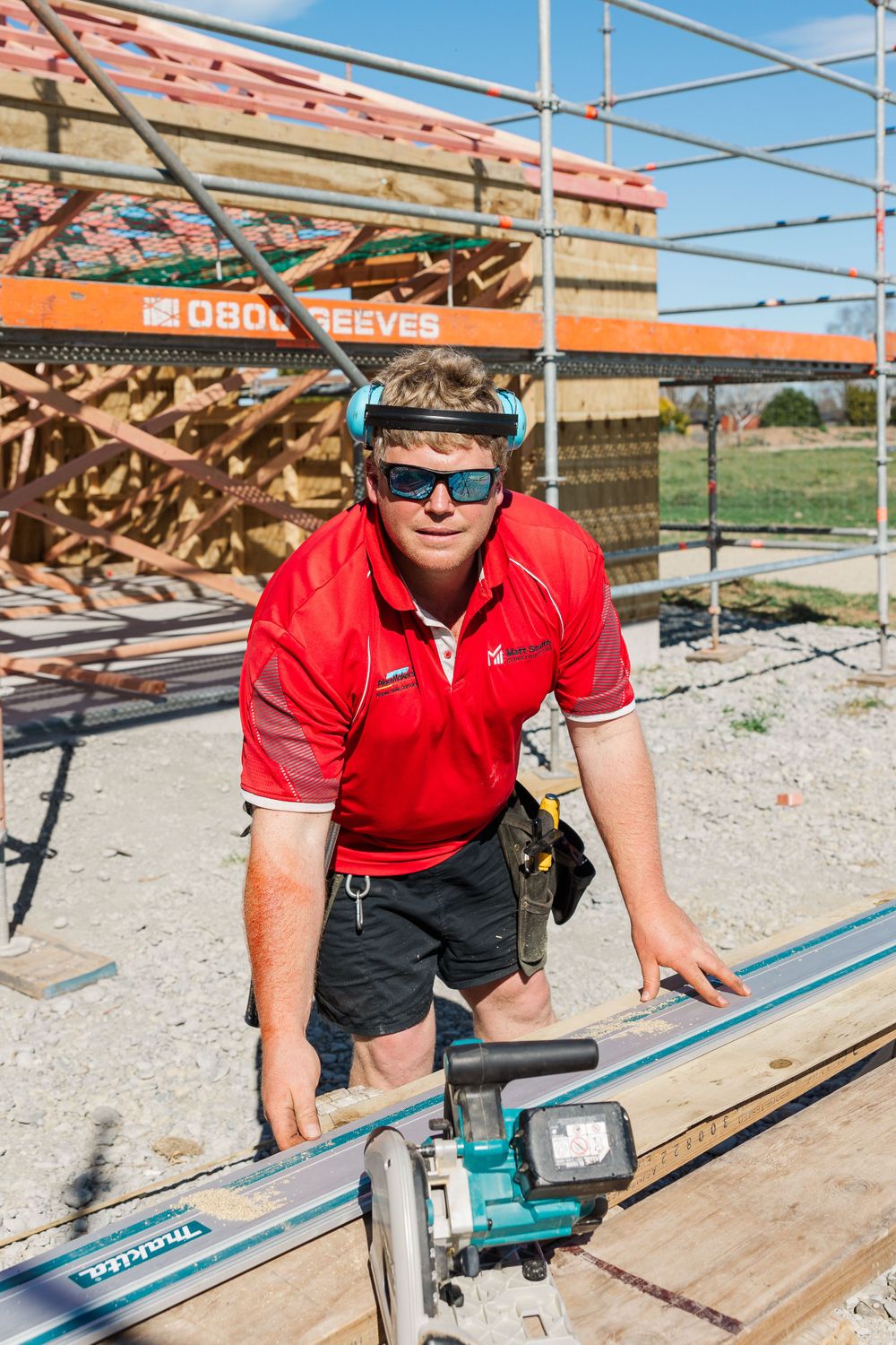 Construction worker with safety gear operating equipment on scaffolding at building site.