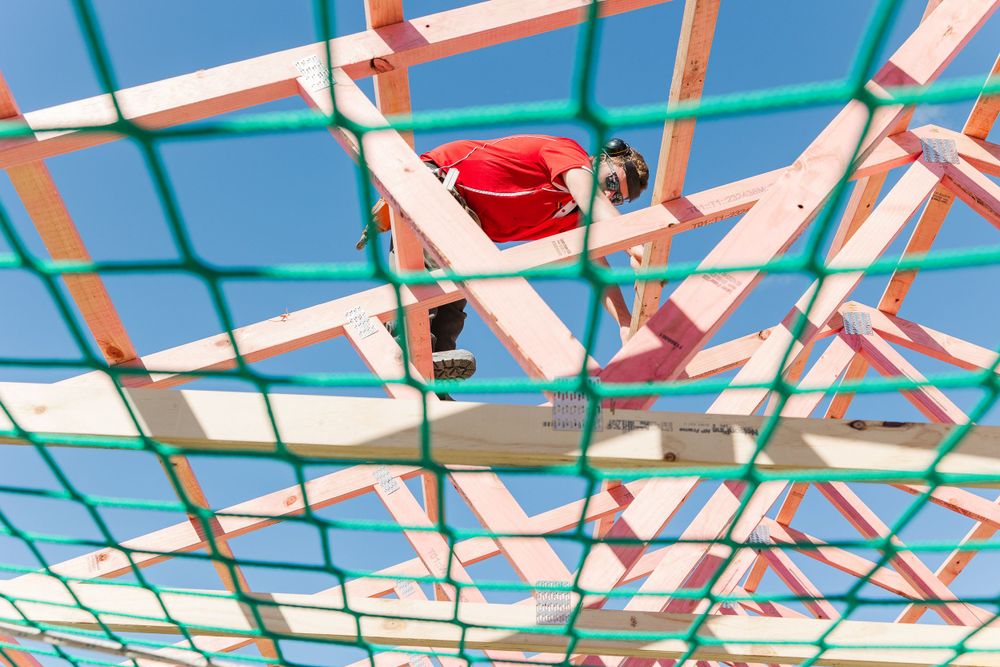Red-painted roof trusses create geometric patterns against a blue sky during construction.