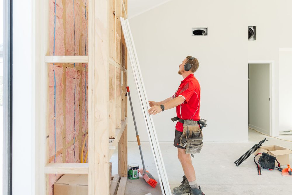 Construction worker in red shirt installing drywall in a residential interior.
