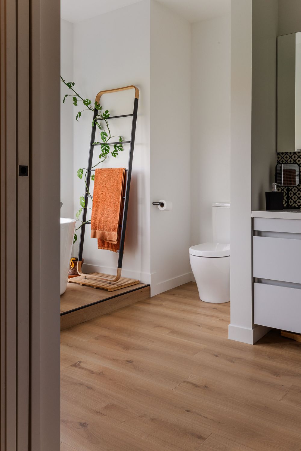 Minimalist bathroom interior with wooden floor mirror and light hardwood flooring.