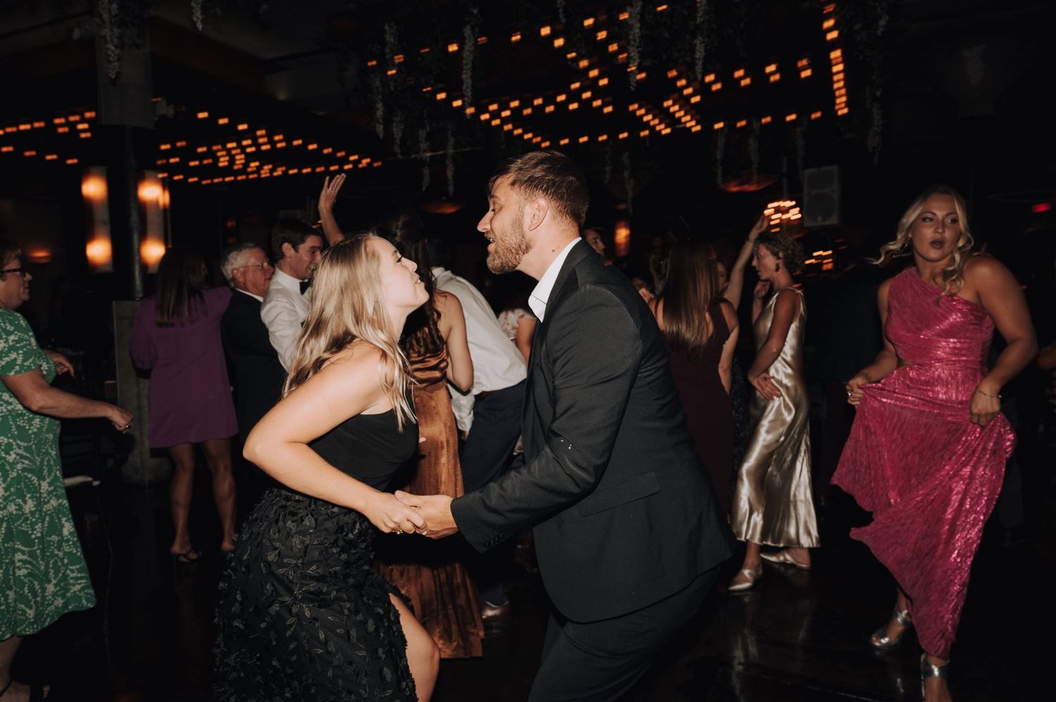 Guests dancing energetically under mood lighting at evening celebration event.