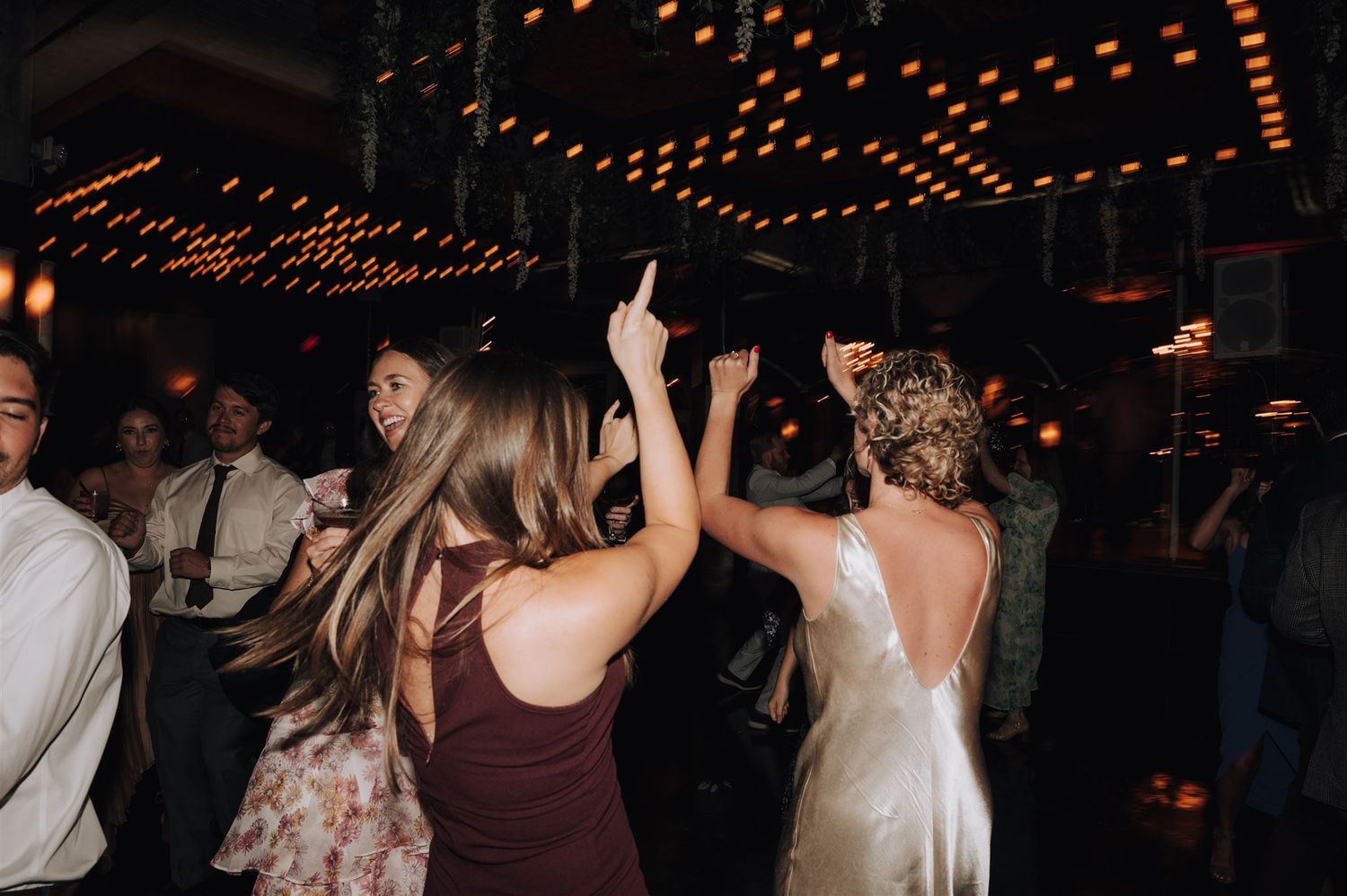 Guests dancing with raised arms under string lights at nighttime celebration.