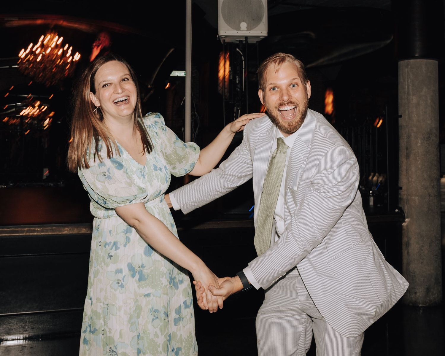 Couple dancing playfully together at an indoor reception with string lights and industrial decor.