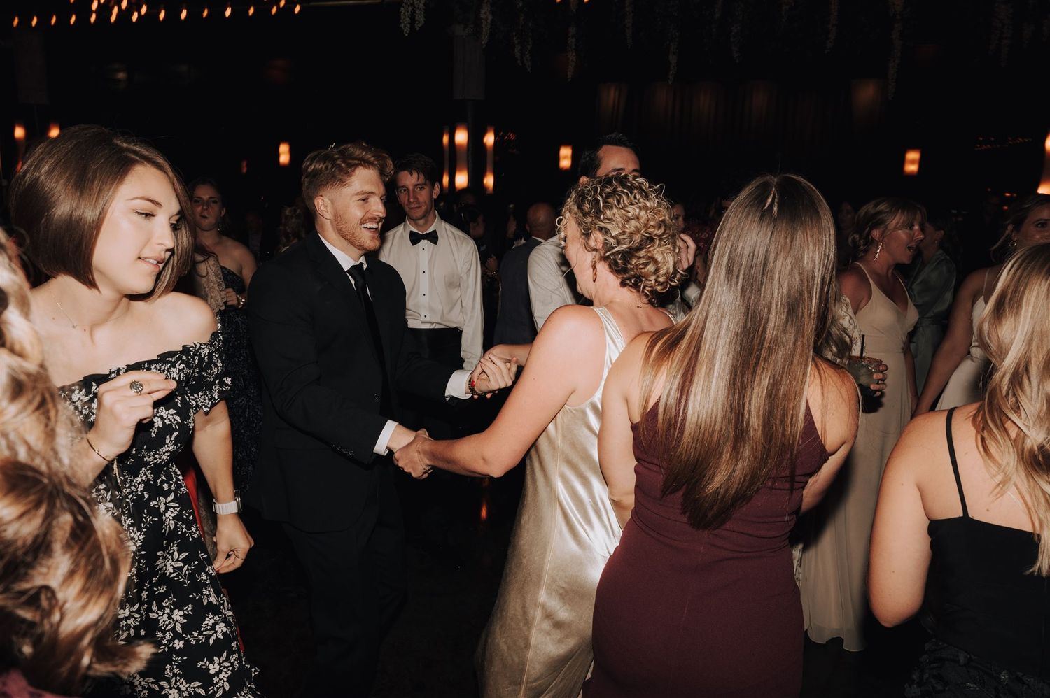 Guests dancing and socializing at an elegant evening event under decorative lighting.