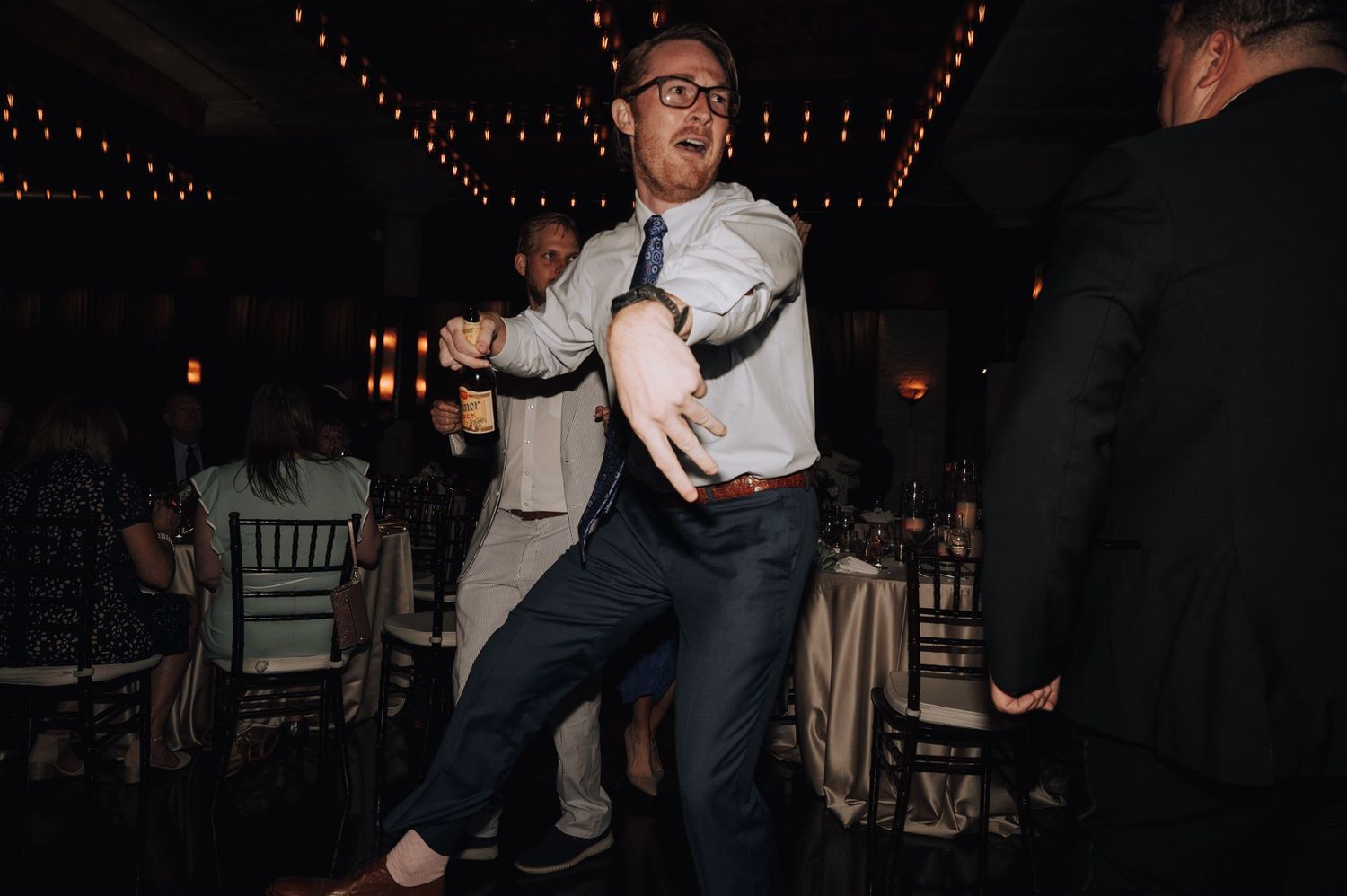 Guest showing off enthusiastic dance moves at a formal event under string lights.