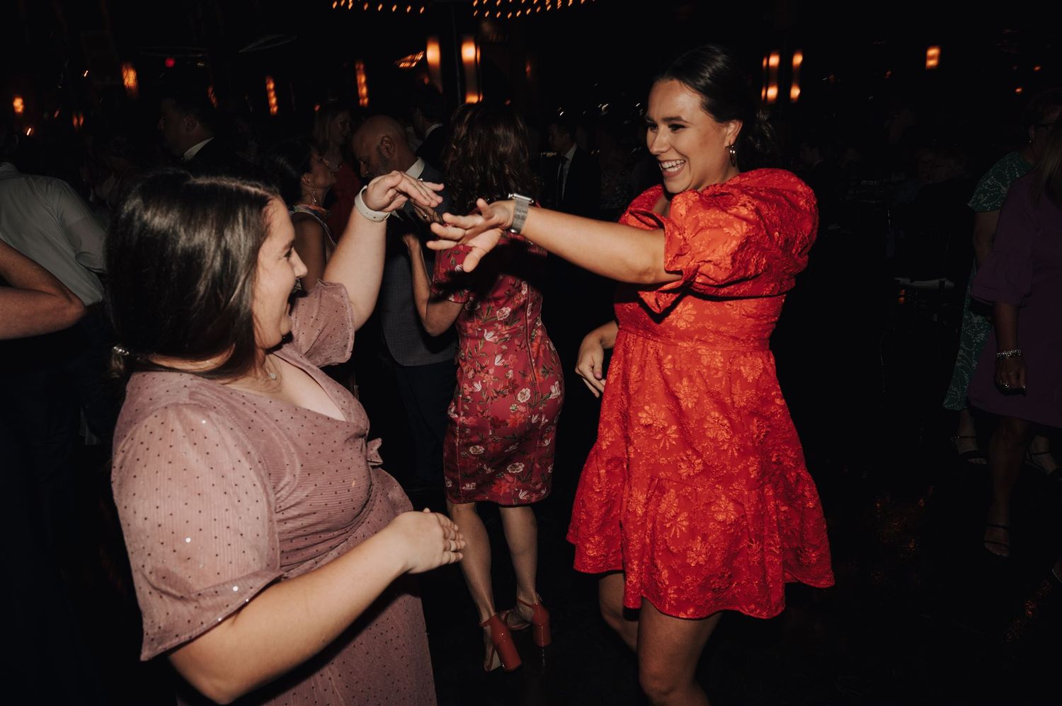 Party guests dancing energetically under dim lighting with festive dresses and lively expressions.