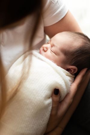 A peaceful sleeping newborn baby wrapped in a white blanket being held.