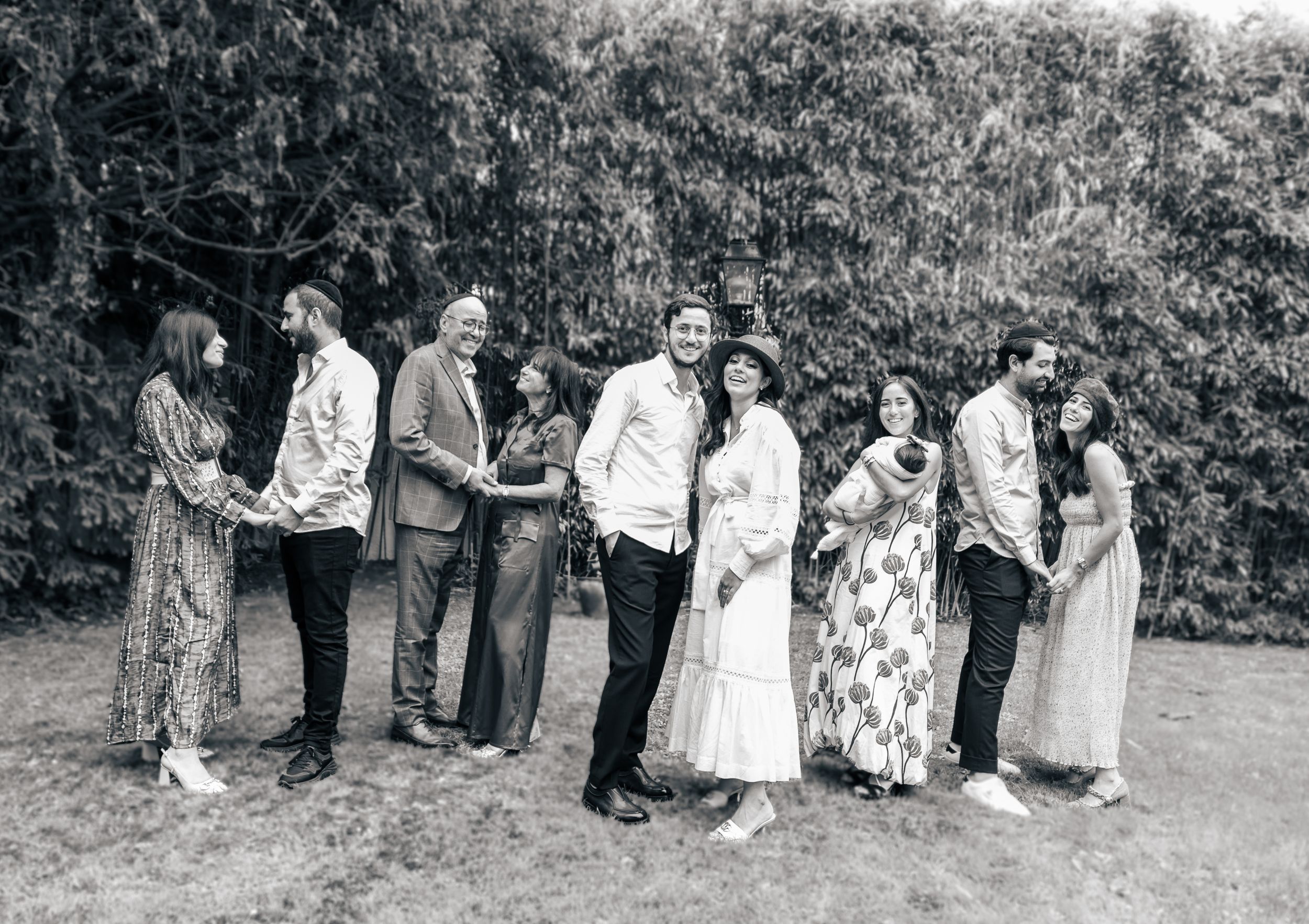 Black and white photo of a wedding party posing together in front of a hedge.