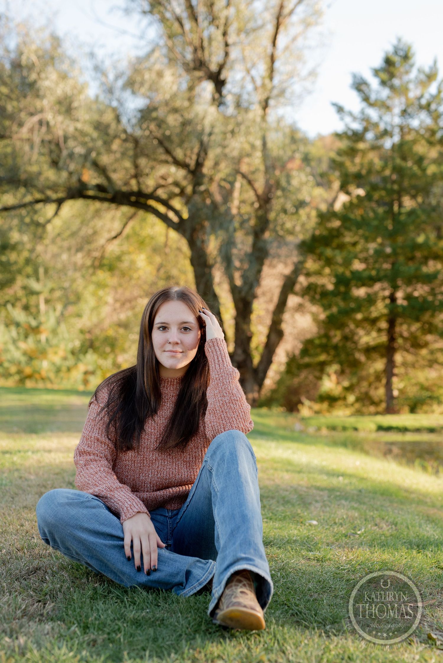 Casual autumn portrait in a cozy sweater taken in a peaceful park setting with tall trees.