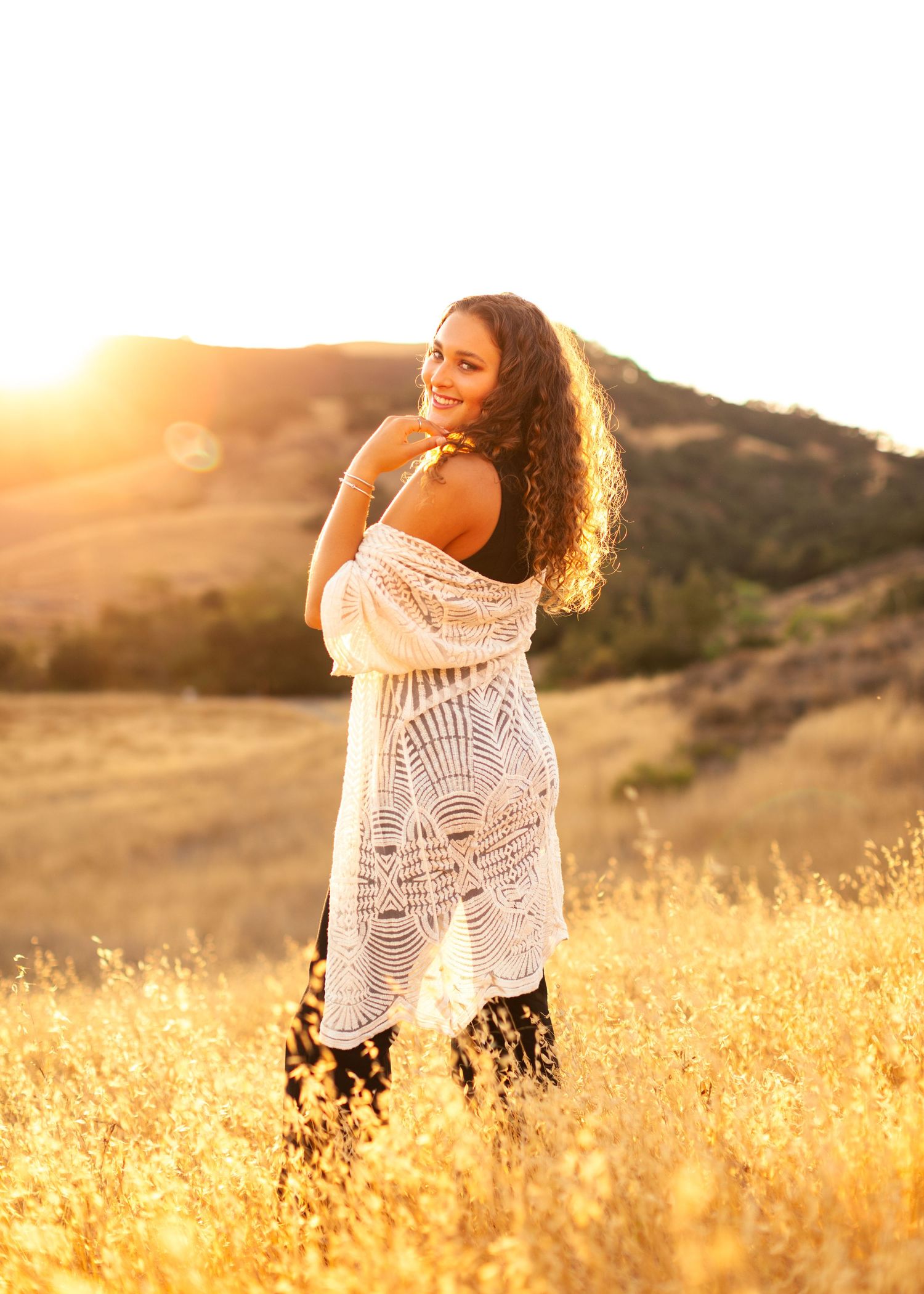 Woman in white crochet dress poses in golden field during sunset.